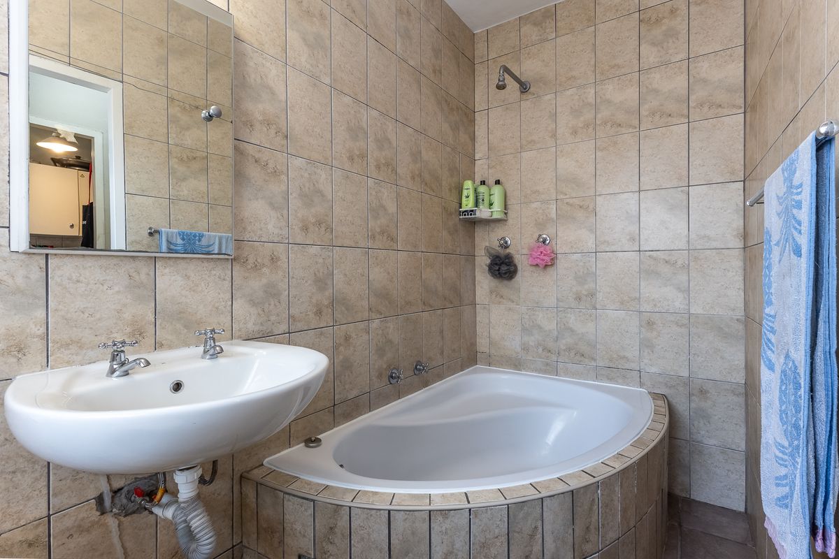 A functional bathroom featuring a built-in bathtub, wall-mounted basin, and neutral tiled finishes throughout.