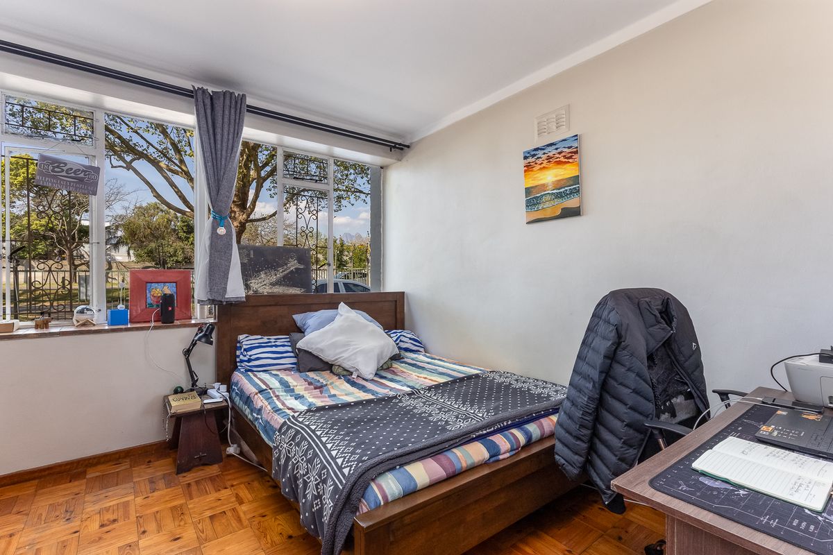 A bedroom featuring classic parquet flooring and a large window that provides natural light and views of the surrounding area.