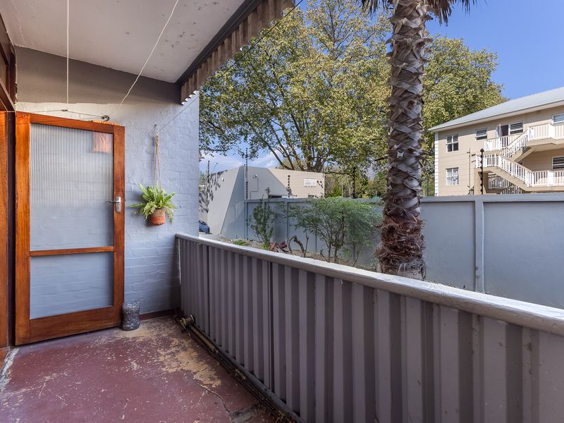 A covered balcony area featuring a timber-framed door and corrugated metal balustrade, overlooking a shared garden space.