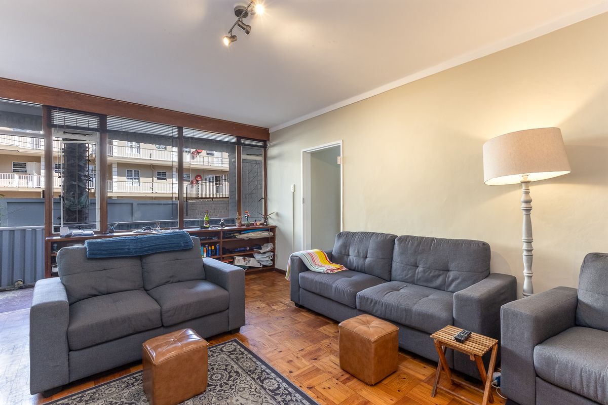 A living room featuring original parquet flooring, large windows providing natural light, and built-in shelving units.