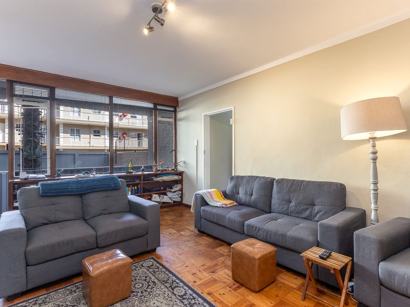 A living room featuring original parquet flooring, large windows providing natural light, and built-in shelving units.