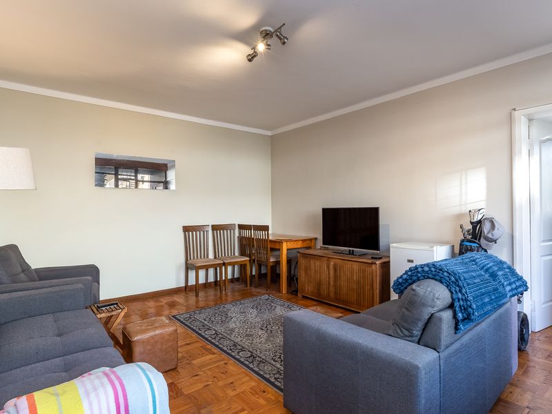 A living room featuring classic parquet flooring, neutral walls, and coved ceiling details, providing a functional and well-lit space.