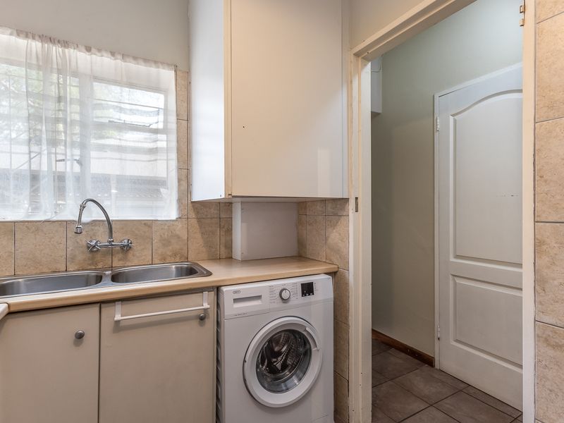 Functional laundry area featuring a double basin sink, built-in cabinetry, tiled splashback, and space for a washing machine.