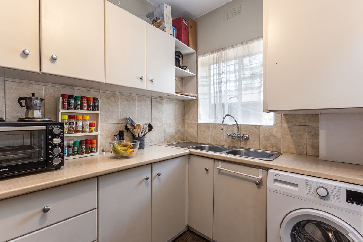 A functional kitchen featuring laminate countertops, a double bowl stainless steel sink, tiled backsplash, and ample built-in cabinetry for storage.