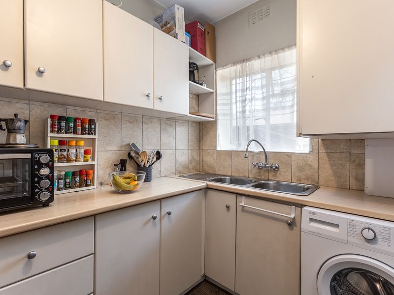 A functional kitchen featuring laminate countertops, a double bowl stainless steel sink, tiled backsplash, and ample built-in cabinetry for storage.