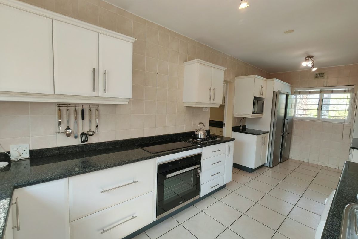 A functional kitchen featuring white cabinetry, dark granite countertops, tiled backsplash, and integrated appliances including an oven and hob.