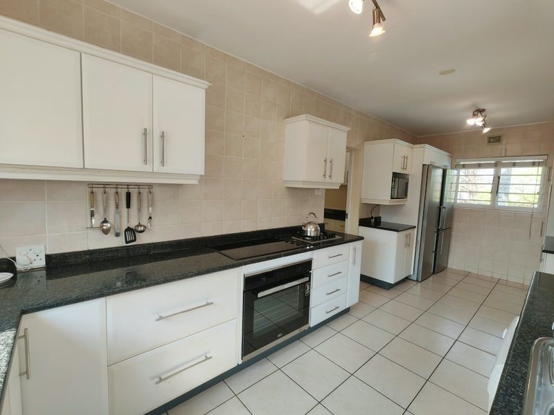 A functional kitchen featuring white cabinetry, dark granite countertops, tiled backsplash, and integrated appliances including an oven and hob.