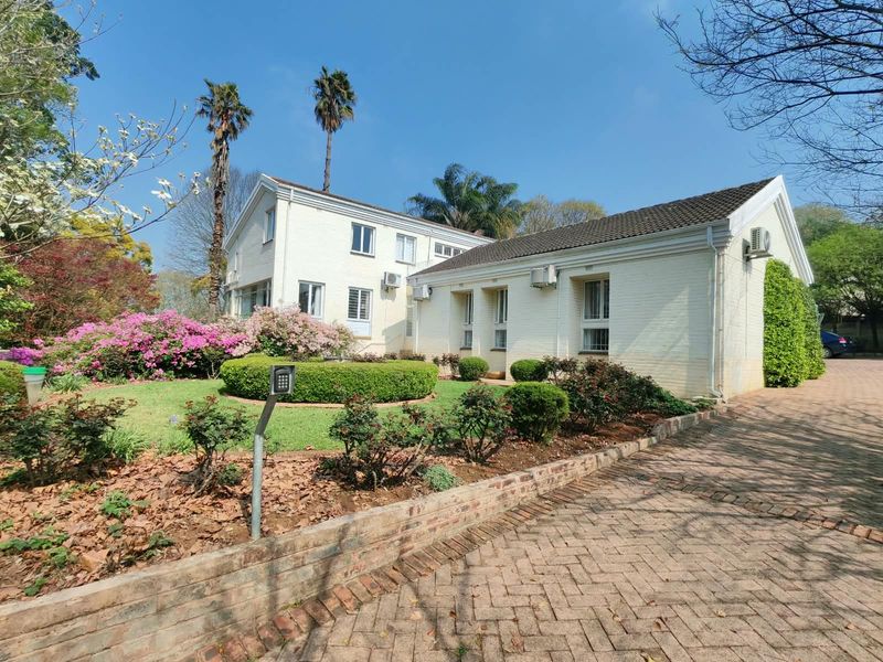 A well-maintained front elevation of a painted brick house featuring a paved driveway, established garden, and multiple split-system air conditioning units.
