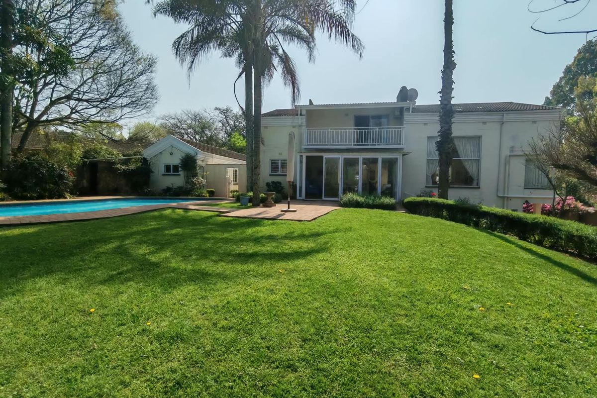 Spacious rear garden featuring a swimming pool, paved patio area, and a two-story residence with a balcony and large sliding glass doors.