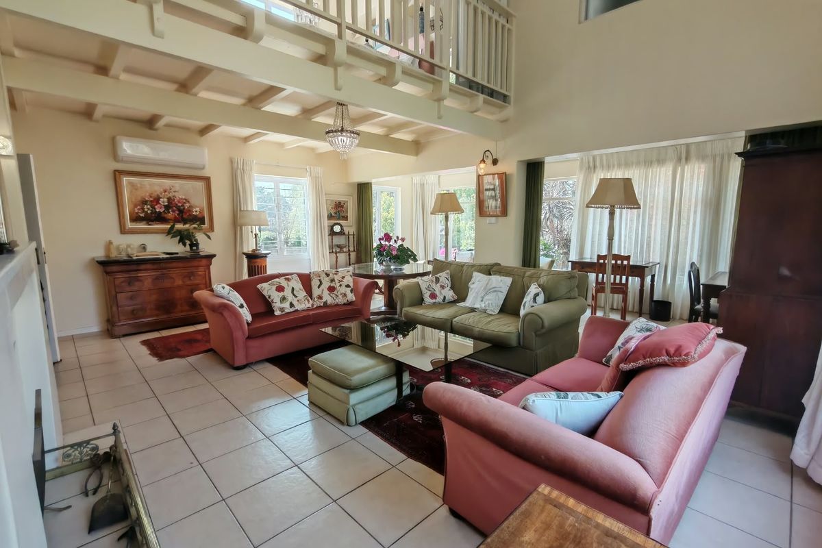 Spacious living room featuring a double-volume ceiling with exposed timber beams, a mezzanine level, tiled flooring, and a fireplace.