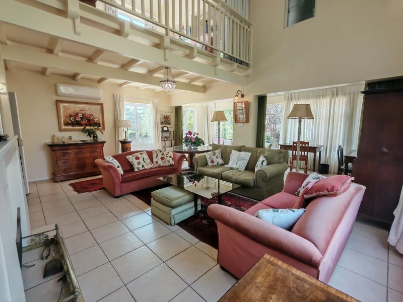 Spacious living room featuring a double-volume ceiling with exposed timber beams, a mezzanine level, tiled flooring, and a fireplace.
