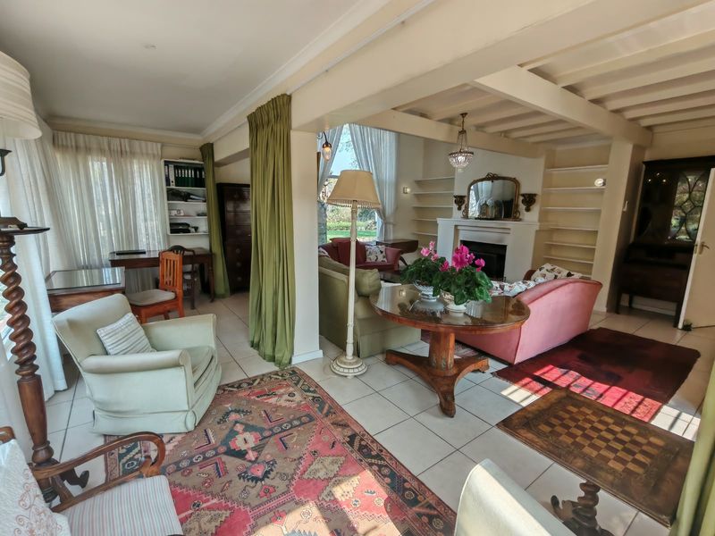 Spacious open-plan living area featuring a fireplace, built-in shelving, and exposed ceiling beams, with large windows providing natural light and garden views.