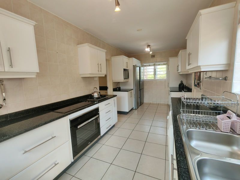 A functional galley-style kitchen featuring white cabinetry, dark granite countertops, tiled flooring, and integrated appliances including an oven and hob.