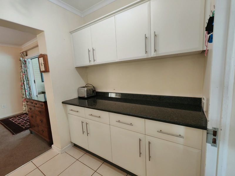 A functional scullery area featuring white built-in cabinetry and a dark granite countertop, providing additional storage and workspace.