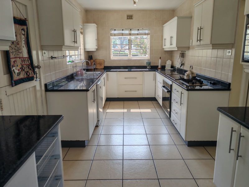 A functional U-shaped kitchen featuring white cabinetry, dark granite countertops, a built-in oven, gas hob, and neutral ceramic floor tiles.