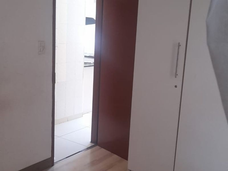 A simple bedroom featuring light-toned laminate flooring and a white built-in wardrobe, with a doorway leading to an adjacent tiled area.