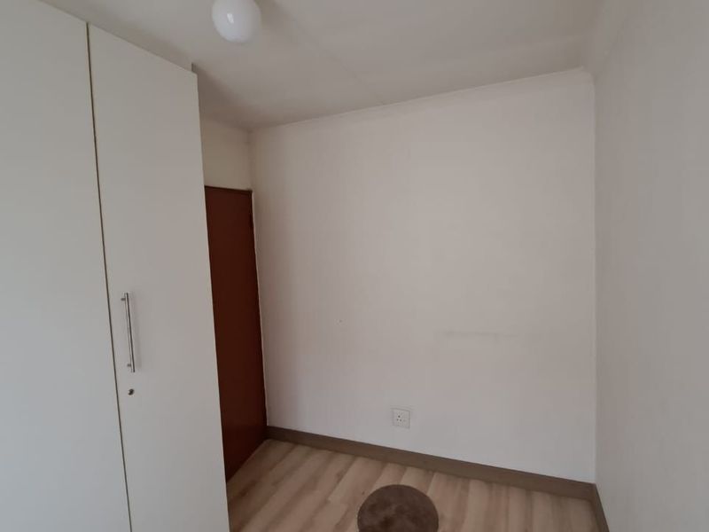 A clean, empty bedroom featuring light-toned laminate flooring and a built-in white wardrobe, offering a neutral space ready for personalization.