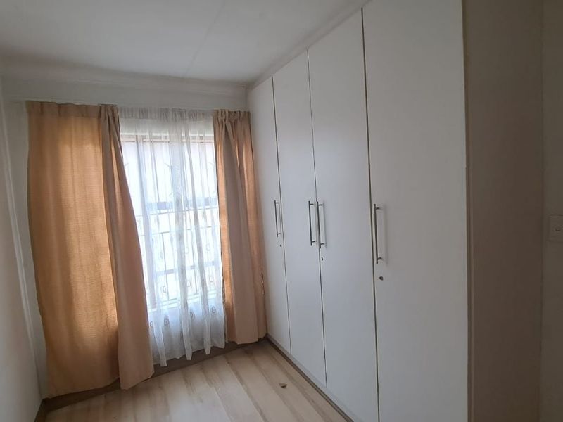 A clean, empty bedroom featuring light-toned laminate flooring and a full wall of white built-in cupboards.