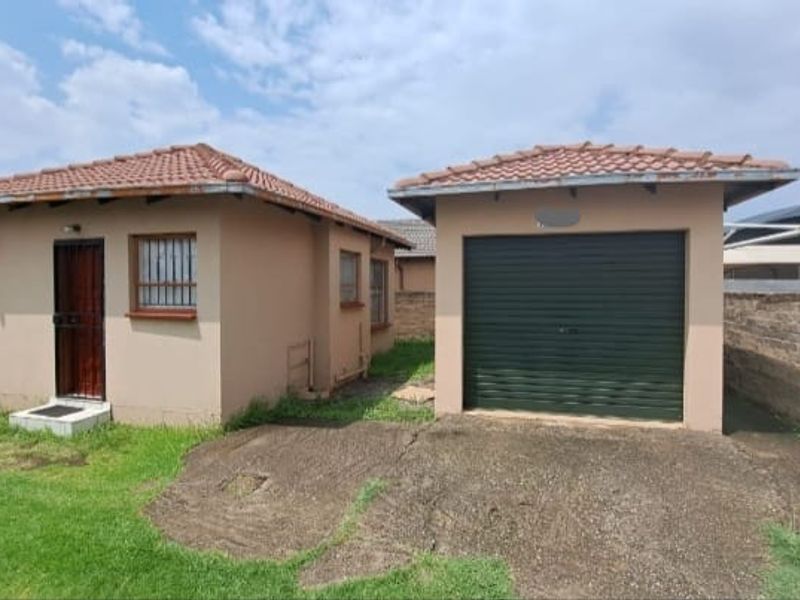 Exterior view of a detached house featuring a tiled roof, security gate, and a single garage with a roll-up door and concrete driveway.