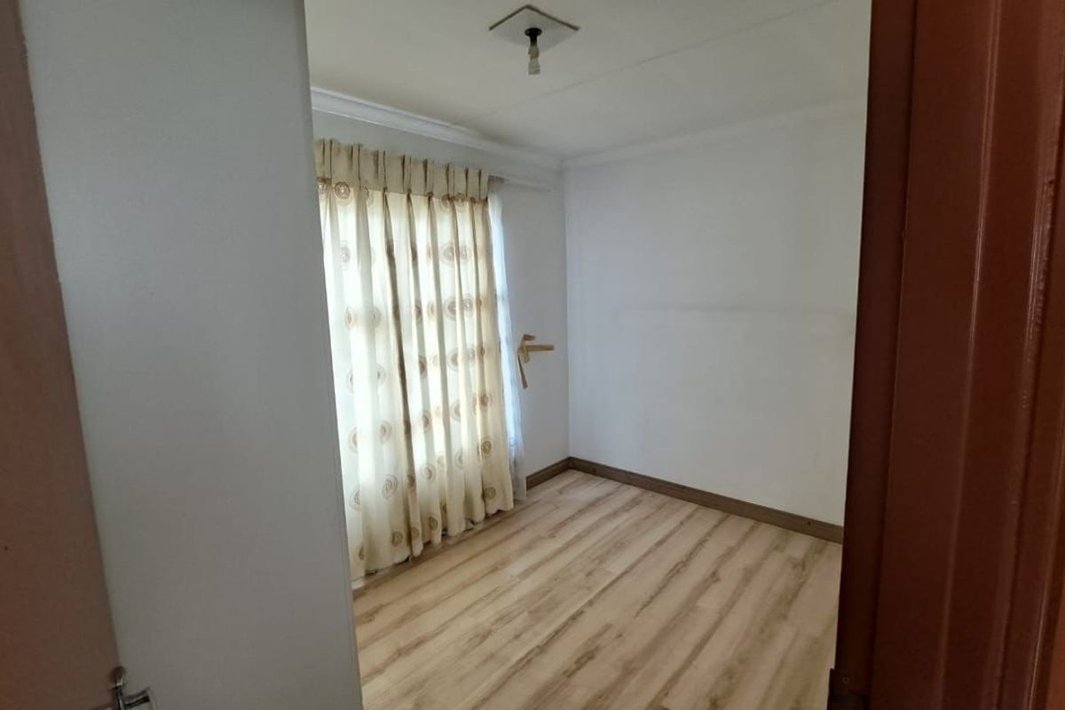 An empty bedroom featuring light-toned laminate flooring, neutral walls, and a window with curtains, offering a blank canvas for personalization.