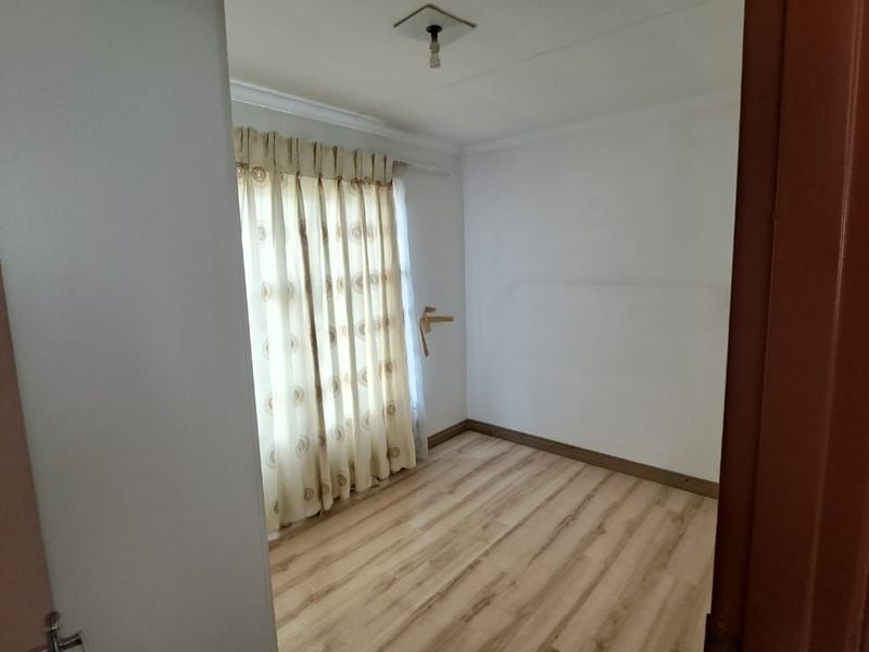 An empty bedroom featuring light-toned laminate flooring, neutral walls, and a window with curtains, offering a blank canvas for personalization.