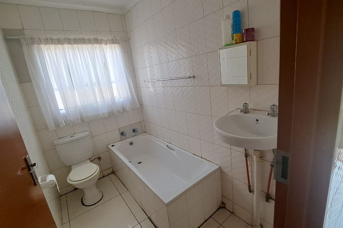 A functional bathroom featuring a bathtub, toilet, and pedestal basin with fully tiled walls and flooring, offering potential for modern renovation.
