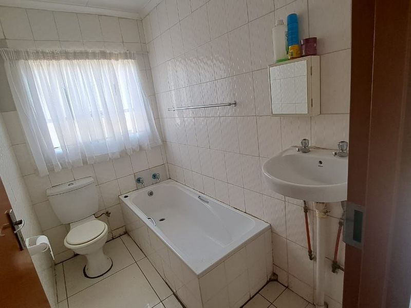 A functional bathroom featuring a bathtub, toilet, and pedestal basin with fully tiled walls and flooring, offering potential for modern renovation.