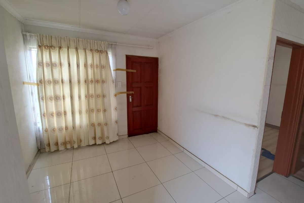 An empty living room featuring tiled flooring, a timber door, and neutral walls, presenting a blank canvas for renovation or interior design updates.
