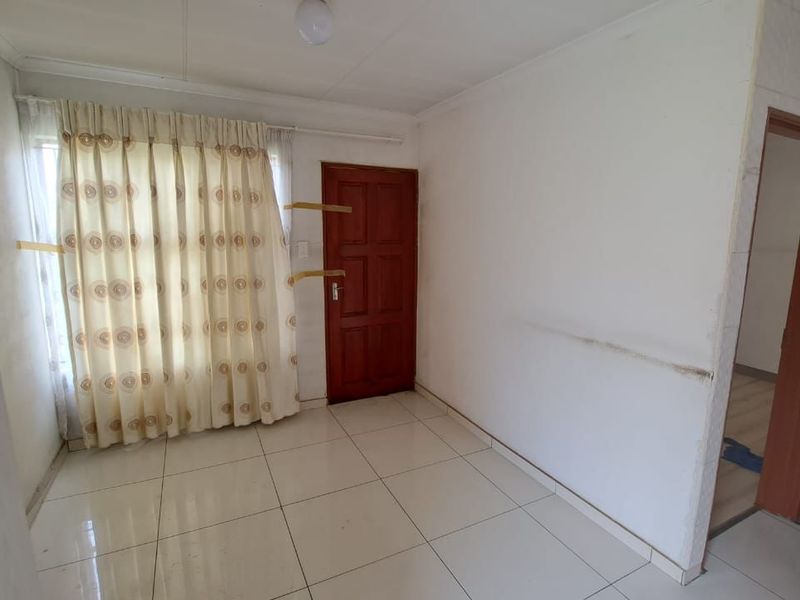 An empty living room featuring tiled flooring, a timber door, and neutral walls, presenting a blank canvas for renovation or interior design updates.
