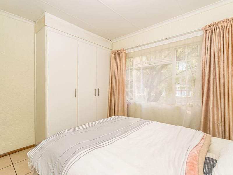A functional bedroom featuring built-in cupboards, tiled flooring, and a window with natural light.