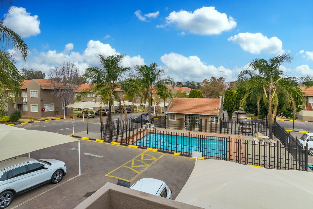 Elevated view of the apartment complex grounds, featuring a communal swimming pool, secure fencing, and paved parking areas with shade cloth carports.