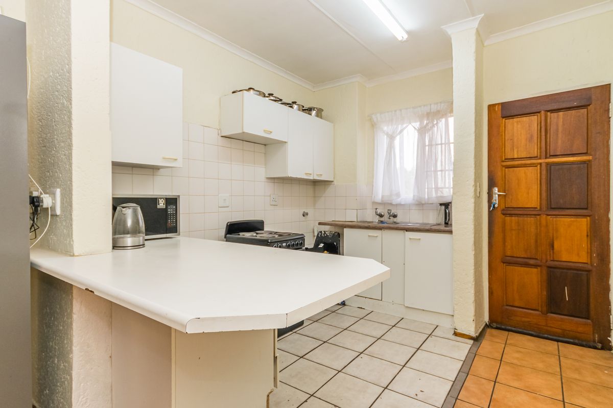 A functional kitchen featuring white cabinetry, laminate countertops, tiled backsplash, and a freestanding stove, with direct access to an exterior wooden door.