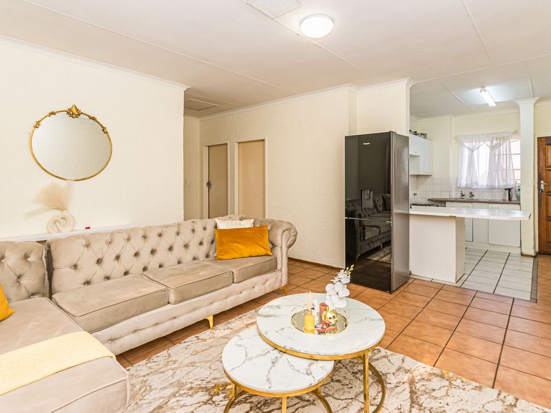 Open-plan living area featuring tiled flooring, a functional kitchen with built-in cabinetry, and direct access to the main entrance.