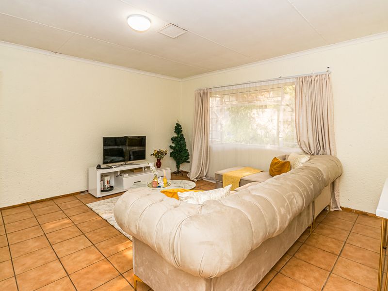A living room featuring tiled flooring and a large window, providing a functional space with potential for modern updates.