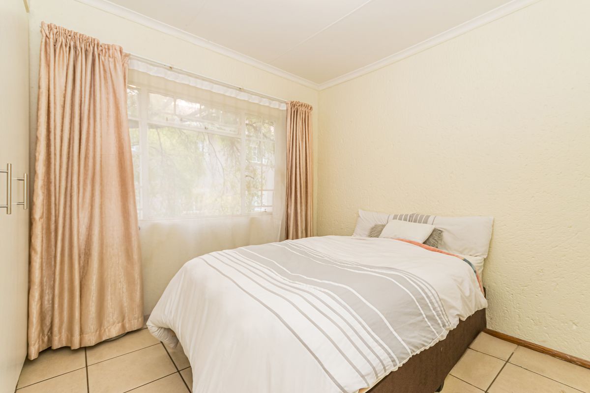 A bedroom featuring tiled flooring, built-in cupboards, and a large window allowing natural light.