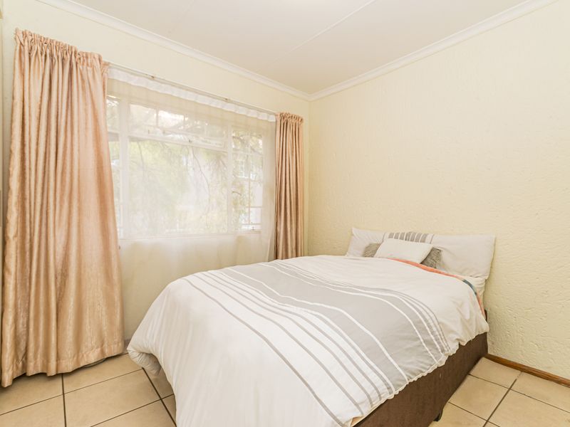 A bedroom featuring tiled flooring, built-in cupboards, and a large window allowing natural light.