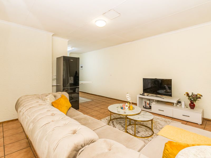 An open-plan living area featuring tiled flooring and neutral walls, providing a functional space that connects to the kitchen area.