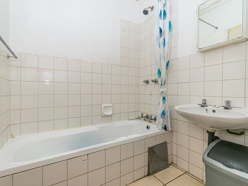 A dated bathroom featuring a standard bathtub with shower attachment, wall-mounted basin, and tiled finishes, requiring cosmetic updates and maintenance.