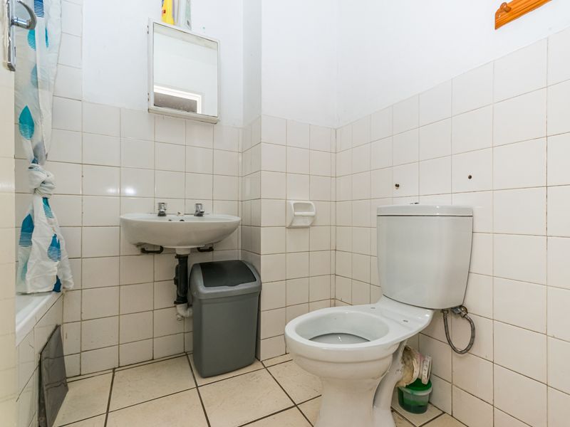 A functional bathroom featuring a wall-mounted basin, standard toilet, and full-height wall tiling, currently requiring cosmetic updates and maintenance to improve its overall condition.
