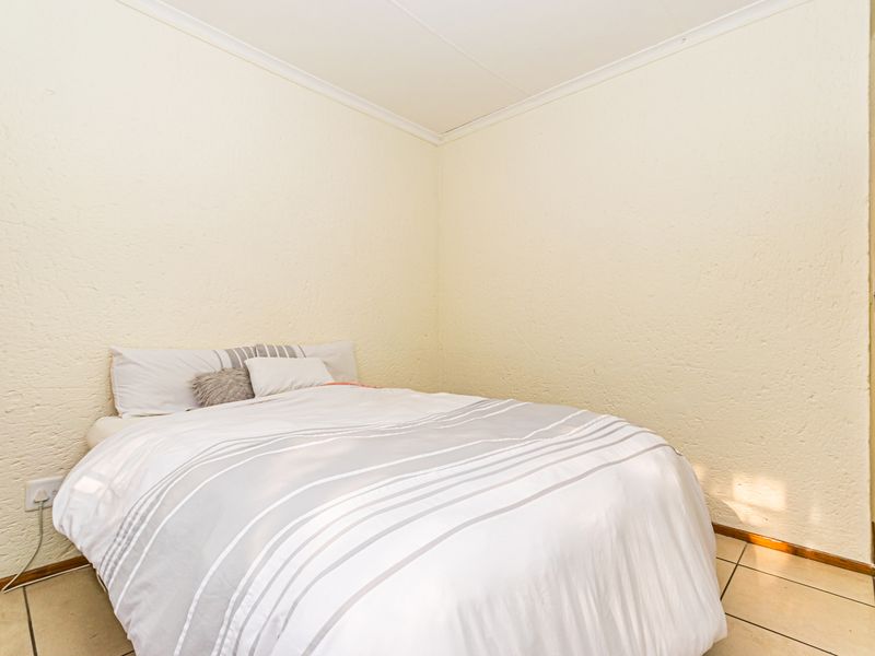 A simple bedroom featuring tiled flooring, textured walls, and coved ceiling detailing, providing a functional and neutral living space.