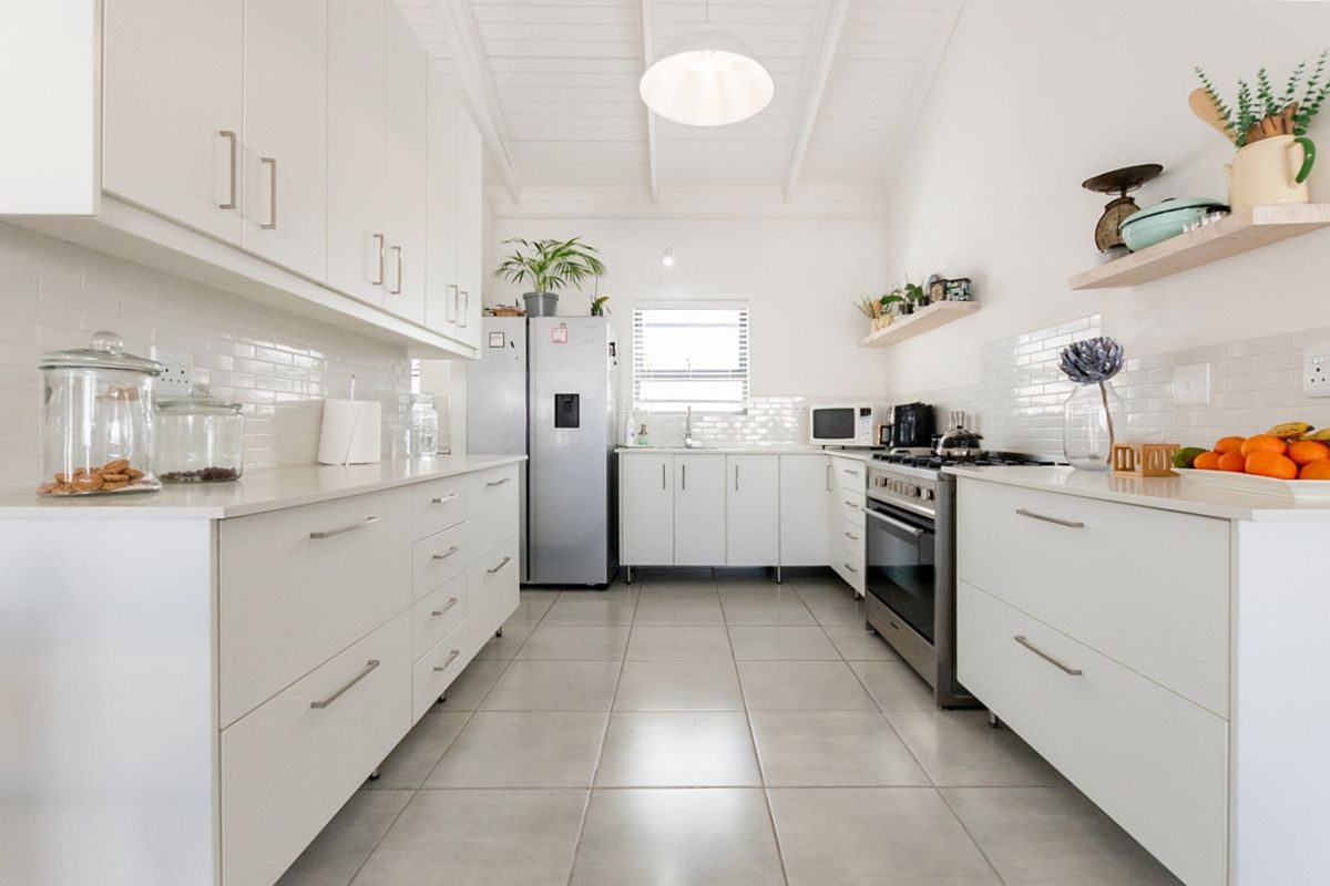 Modern galley-style kitchen featuring white cabinetry, quartz countertops, subway tile backsplash, gas stove, and tiled flooring under an exposed beam ceiling.