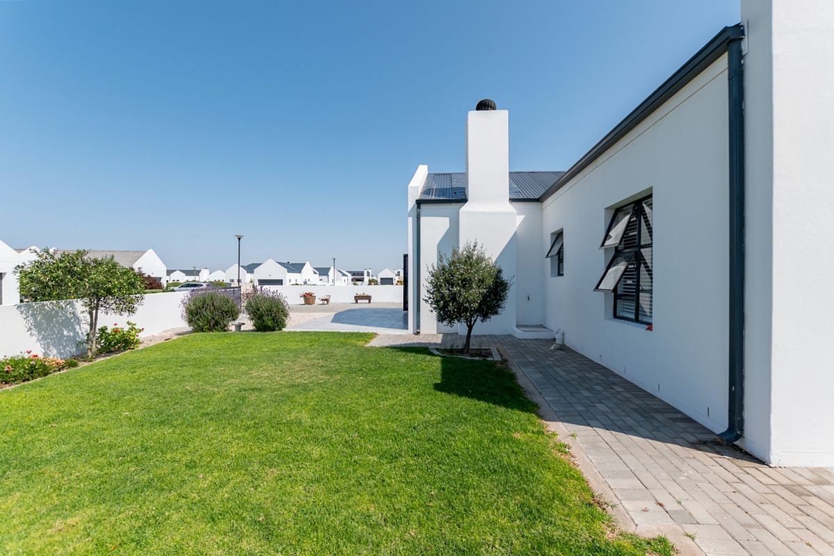A well-maintained rear garden featuring a paved walkway, manicured lawn, and a white exterior facade with a prominent chimney.