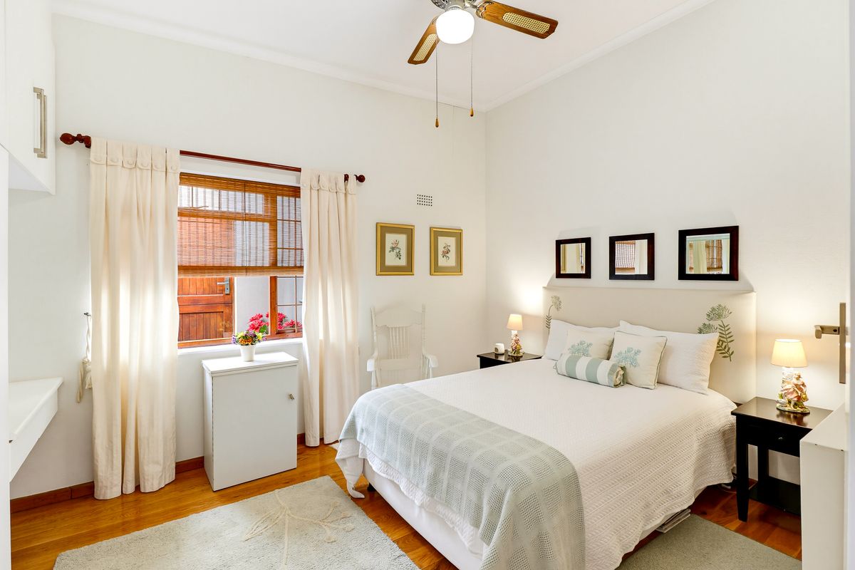 A well-maintained bedroom featuring hardwood flooring, a ceiling fan, and built-in cabinetry, offering a bright and comfortable living space.