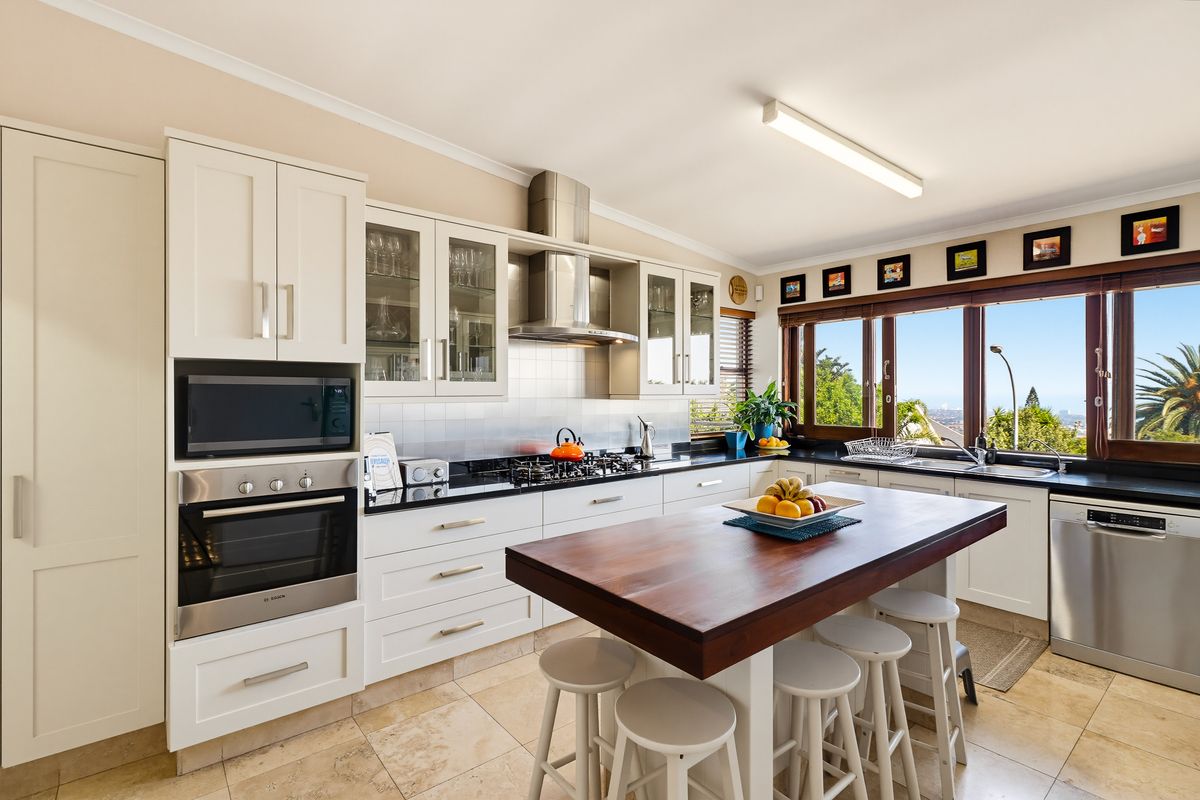 Modern kitchen featuring white shaker cabinetry, stone countertops, a central timber-topped island, built-in appliances, and large windows with scenic views.