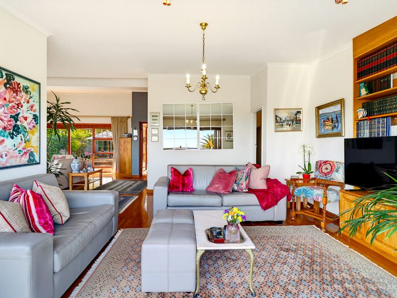 A bright and inviting living room featuring polished hardwood floors, a built-in wooden bookshelf, and a decorative mirror, with seamless flow to the outdoor area.