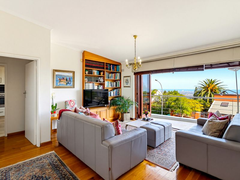 Spacious living room featuring hardwood floors, a custom built-in bookshelf, and large sliding doors opening to a balcony with scenic coastal views.