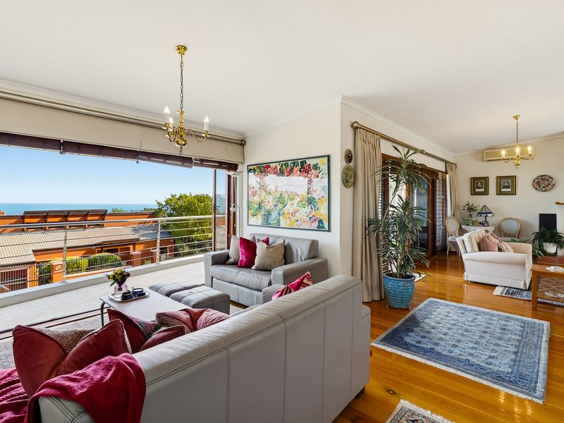 Spacious open-plan living area featuring polished hardwood floors, large sliding doors opening to a balcony with ocean views, and a fireplace.