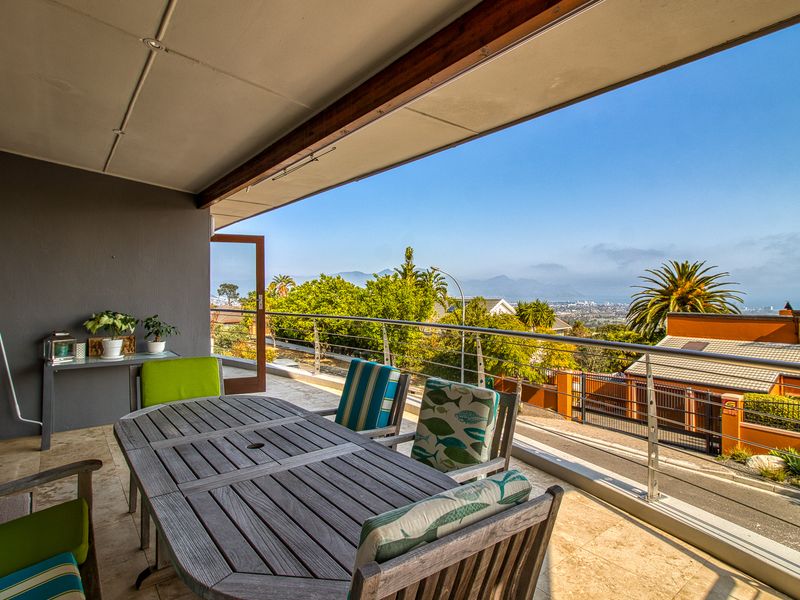 Spacious covered balcony featuring tiled flooring, stainless steel balustrades, and expansive elevated views of the surrounding landscape and coastline.