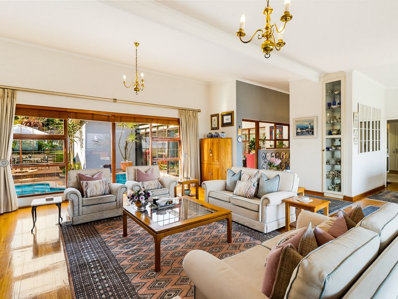 Spacious living room featuring polished hardwood floors, elegant brass chandeliers, and large sliding glass doors providing views of the outdoor pool area.
