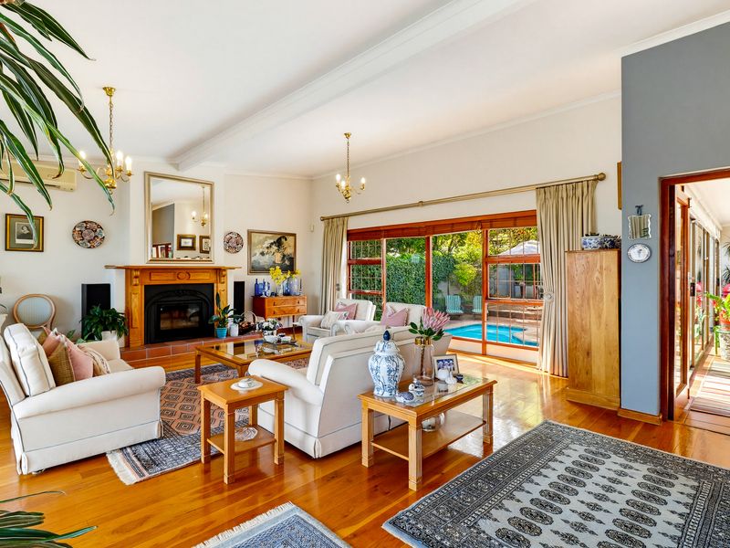 Spacious living room featuring polished wooden flooring, a traditional fireplace with a wooden mantelpiece, and large sliding glass doors opening to the pool area.